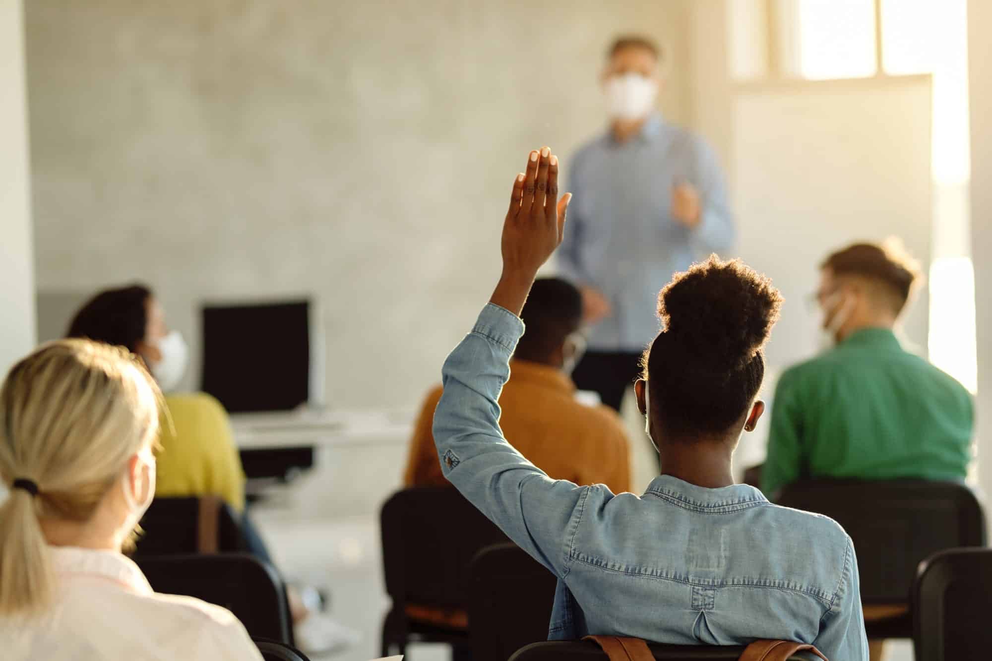 Student raising hand among students in classroom